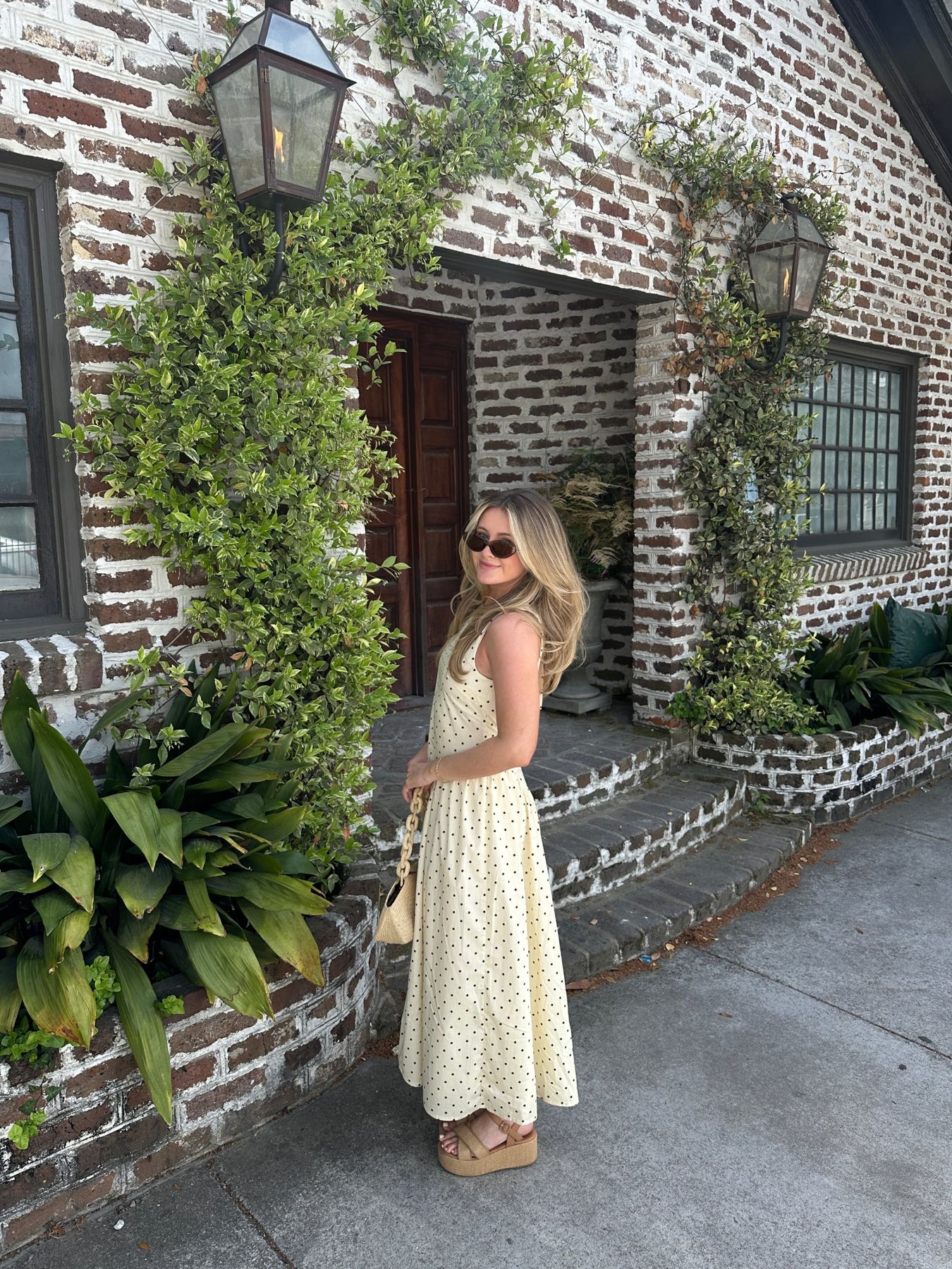 Julia Kane in a yellow polka-dot dress outside a vine-covered brick doorway